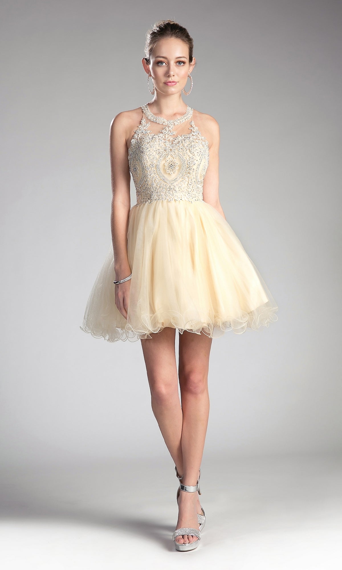 A young woman stands in the High-Neck Short Babydoll Homecoming Dress UJ0119 with an embroidered-lace bodice and tulle skirt, silver heels, and hoop earrings—a stylish, affordable cocktail dress for any occasion.